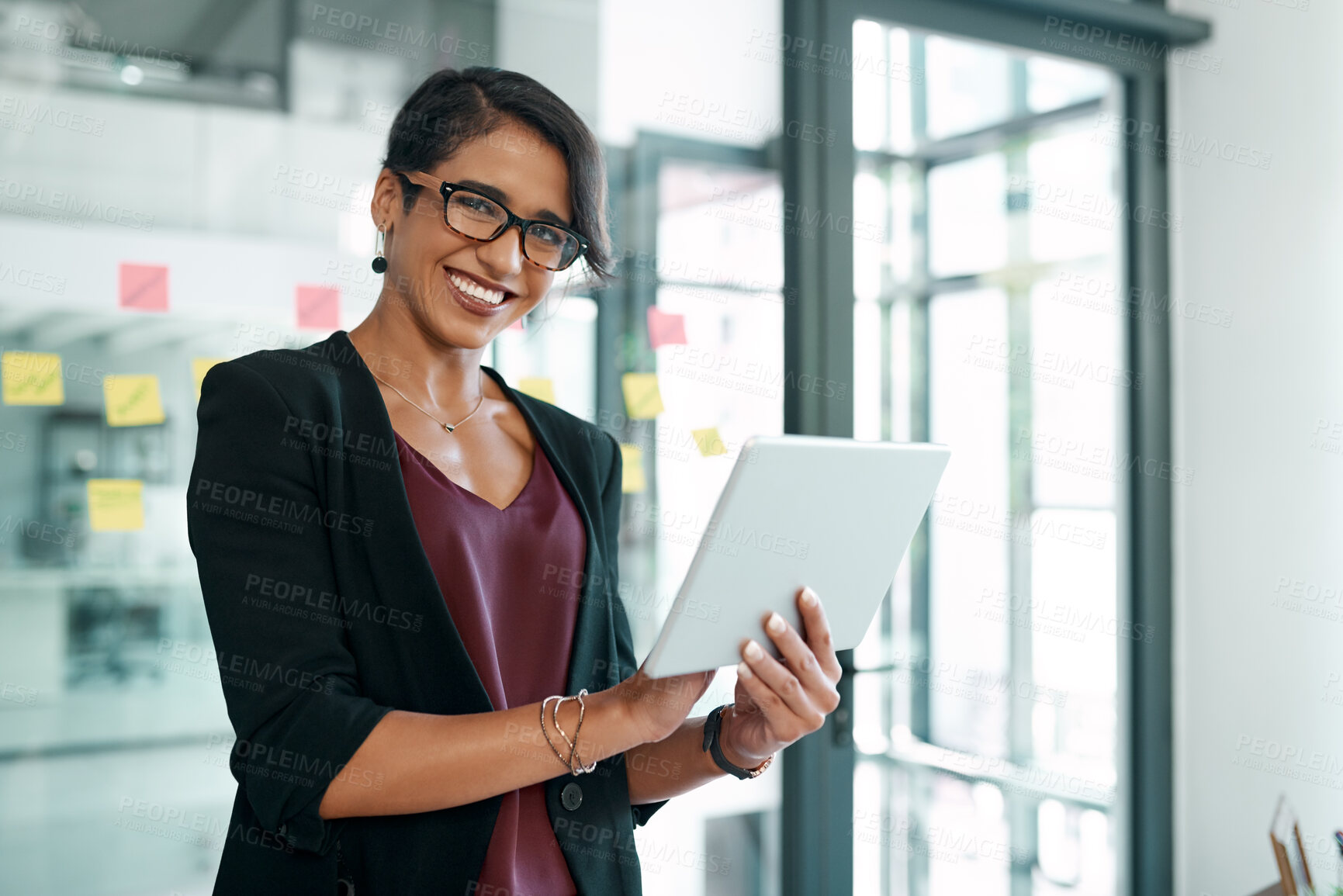 Buy stock photo Shot of an attractive young businesswoman standing alone in the office and using a digital tablet