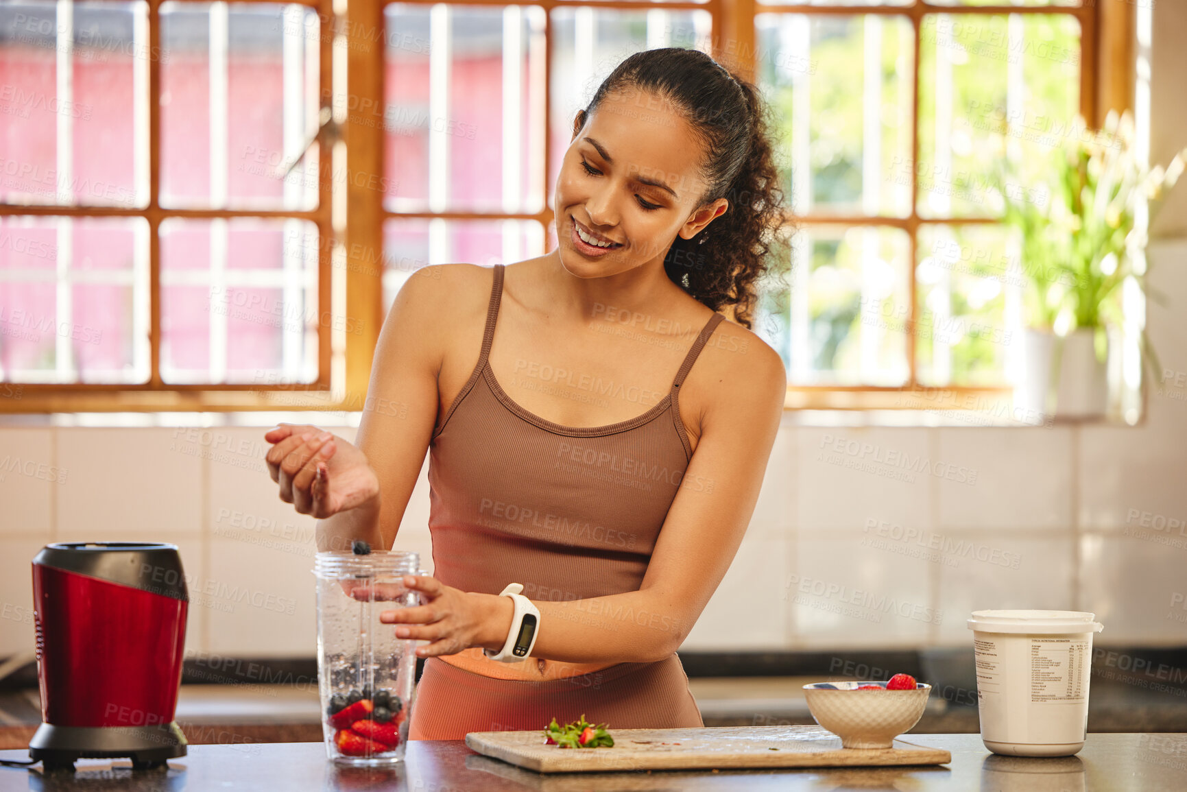 Buy stock photo Shot of an attractive young woman standing alone in her kitchen and preparing a breakfast smoothie