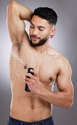 Buy stock photo Shot of a man spraying deodorant into his armpits against a studio background