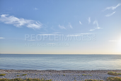 Buy stock photo Seascape view of nature on the coast of a beach and ocean water on a Sunny Summer day. Beautiful scenery of a sea shore filled with grassy, rocky sand textures and the blue sky on the horizon.