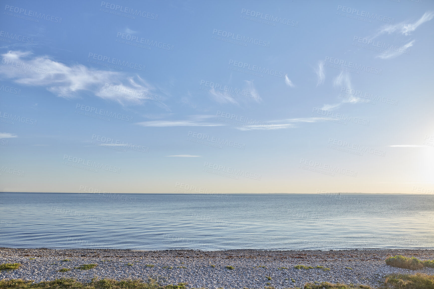 Buy stock photo Seascape view of nature on the coast of a beach and ocean water on a Sunny Summer day. Beautiful scenery of a sea shore filled with grassy, rocky sand textures and the blue sky on the horizon.