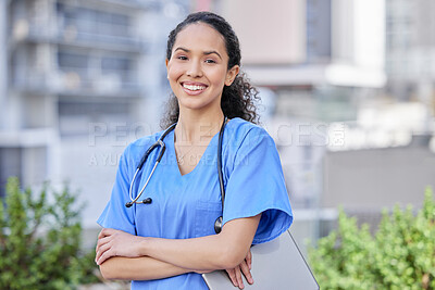 Buy stock photo Shot of a young female doctor standing with her arms crossed against a city background