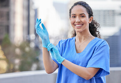 Buy stock photo Shot of a young female doctor putting on gloves against a city background