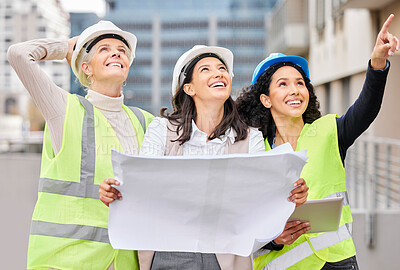 Buy stock photo Cropped shot of three attractive female engineers reading a blueprint while working on a construction site