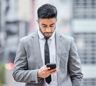 Buy stock photo Shot of a young businessman using his smartphone while walking outside