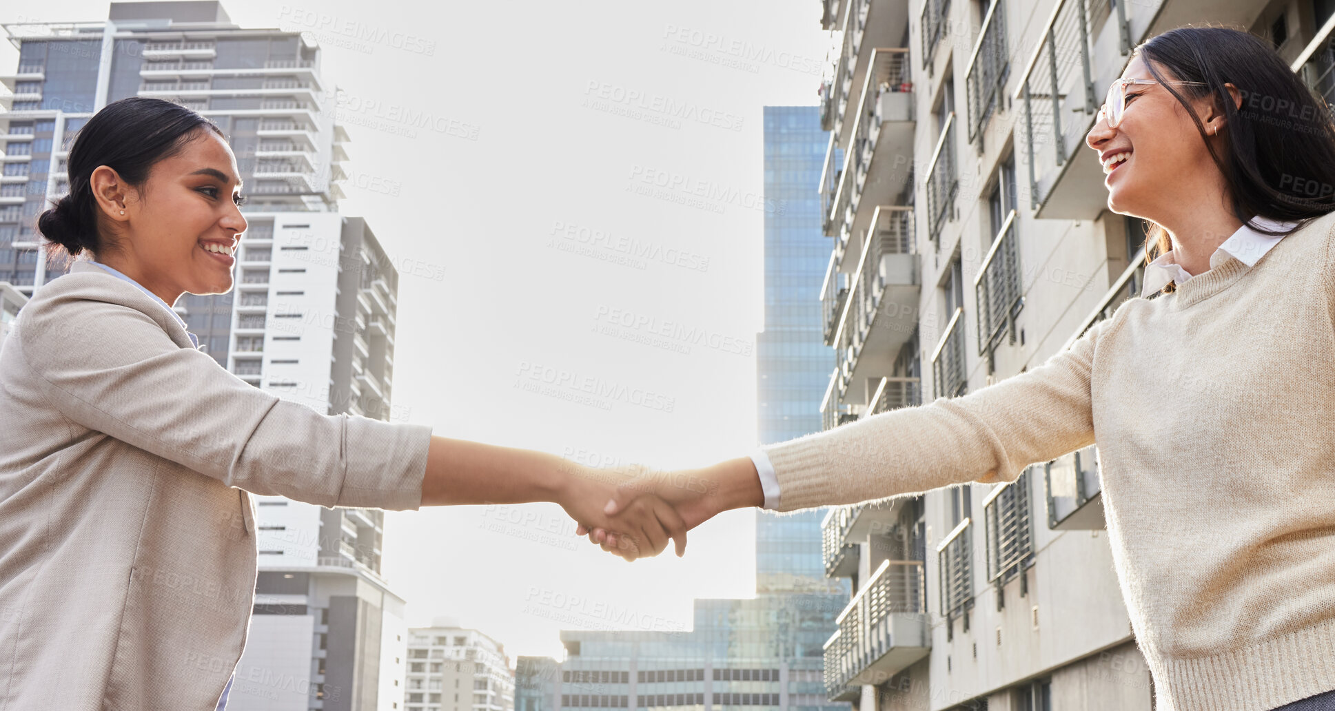 Buy stock photo Cropped shot of two attractive young businesswomen shaking hands on an office balcony