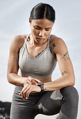 Buy stock photo Shot of a sporty young woman checking her smartwatch while exercising outdoors