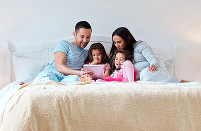 Buy stock photo Shot of a couple and their two daughters lying together on a bed while watching something on a digital tablet