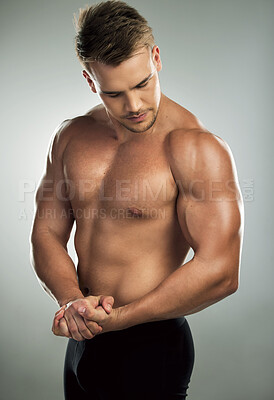Buy stock photo Studio shot of a muscular young man flexing his arm against a grey background