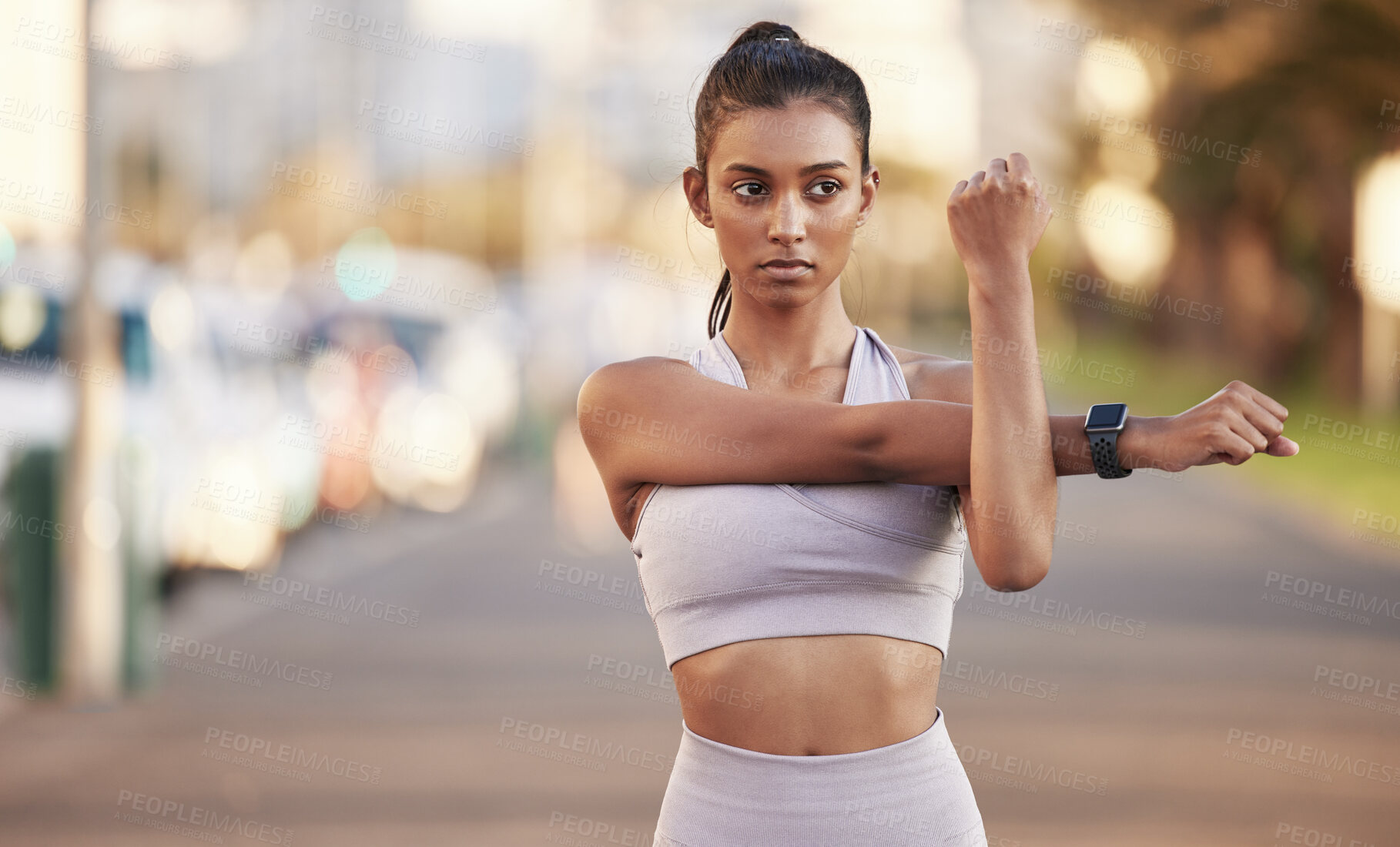 Buy stock photo Shot of a sporty young woman stretching her arms while exercising outdoors