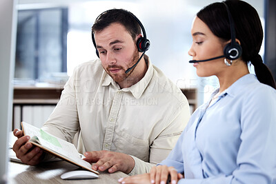 Buy stock photo Call center, colleagues reading a notebook and headset at their desk in a modern office. Collaboration or teamwork, partnership or support and help with coworkers with a book together at workstation