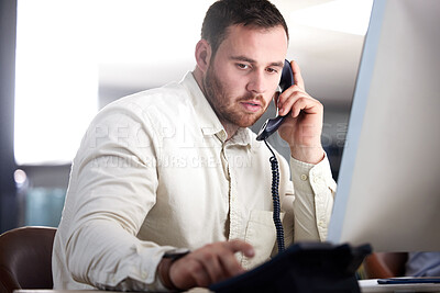 Buy stock photo Shot of a handsome young businessman sitting alone in his office and using a telephone
