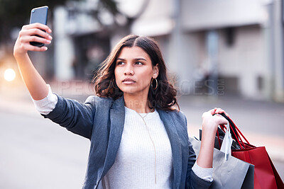 Buy stock photo Shot of a young woman taking a selfie while standing outside with shopping bags