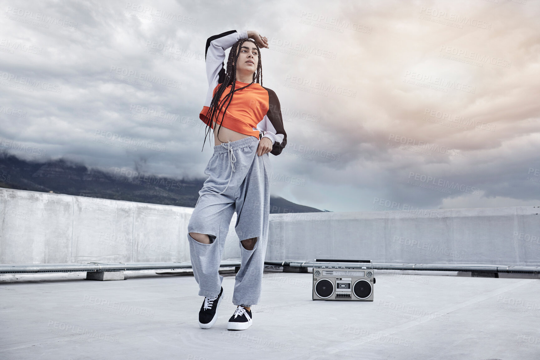 Buy stock photo Full length shot of an attractive young woman dancing on a rooftop against a stormy backdrop