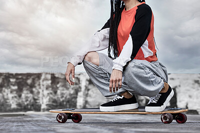 Buy stock photo Cropped shot of an unrecognizable young female skater crouching on her longboard on a rooftop against a stormy backdrop