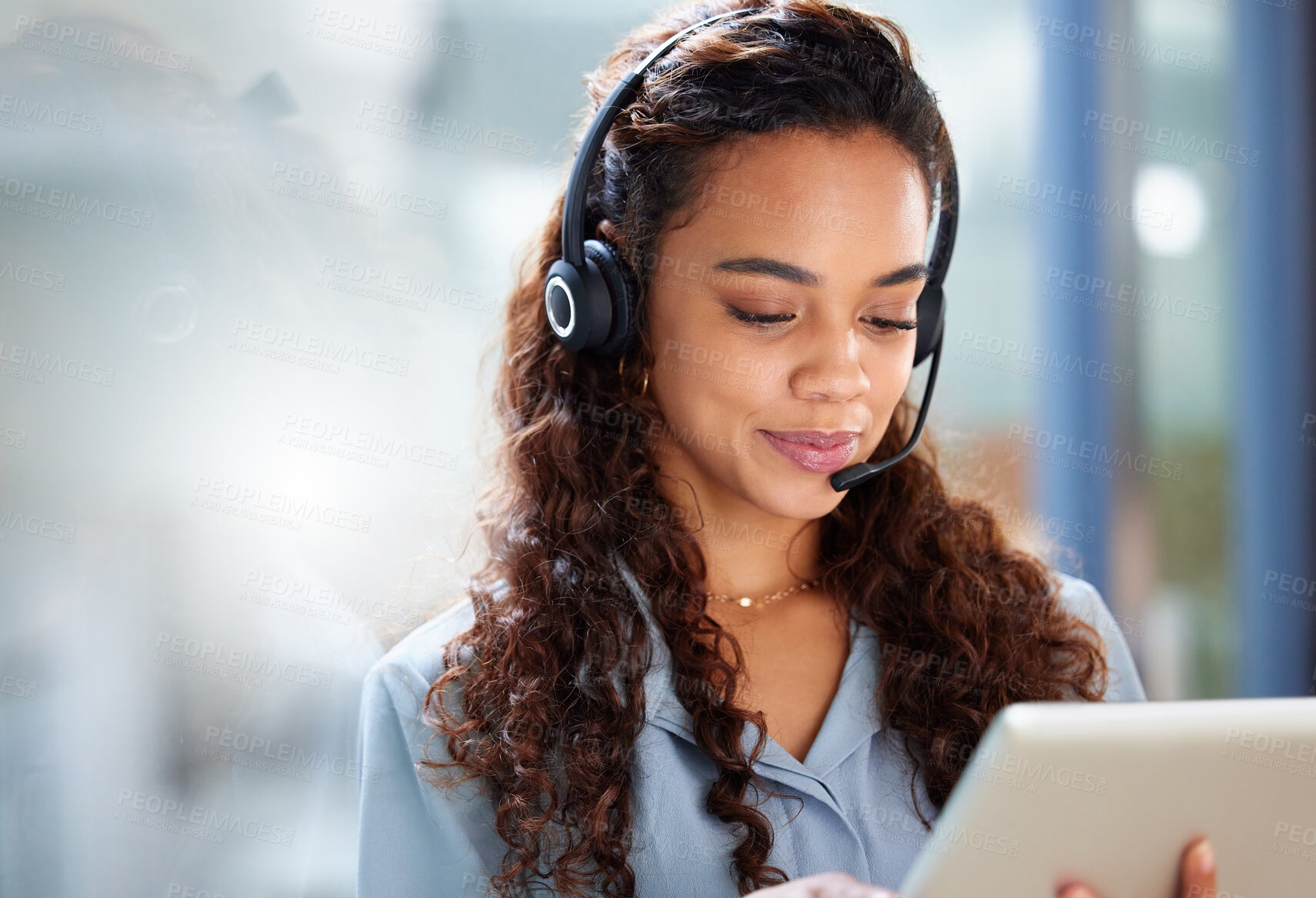 Buy stock photo Cropped shot of an attractive young female call center agent working on her tablet while standing in the office