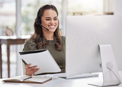 Buy stock photo Shot of a young call centre agent going through paperwork while working on a computer in an office
