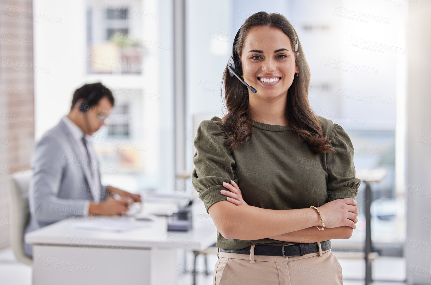 Buy stock photo Portrait of a young call centre agent standing with her arms crossed in an office with her colleague in the background