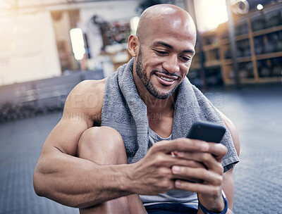 Buy stock photo Shot of a muscular young man using a cellphone while taking a break from exercising in a gym