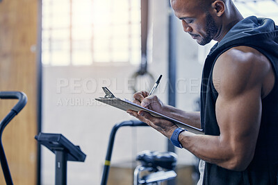 Buy stock photo Shot of a muscular young man writing notes on a clipboard while working in a gym