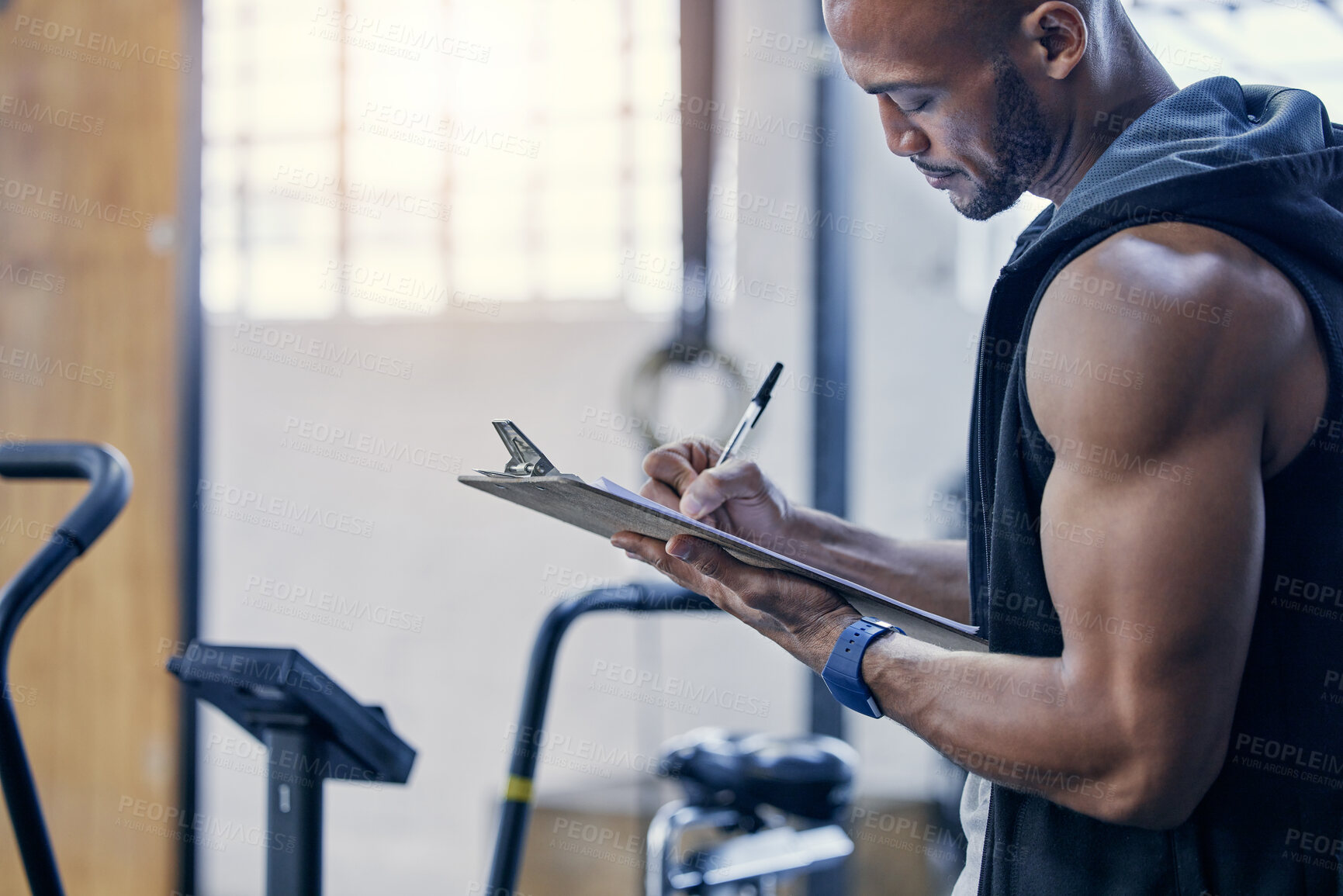 Buy stock photo Shot of a muscular young man writing notes on a clipboard while working in a gym