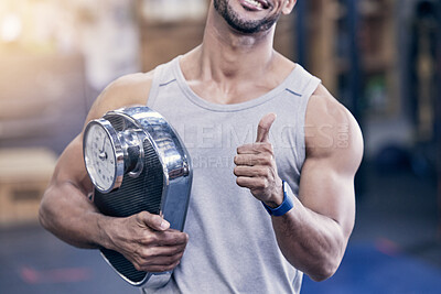 Buy stock photo Closeup shot of a muscular young an holding a scale and showing thumbs up in a gym