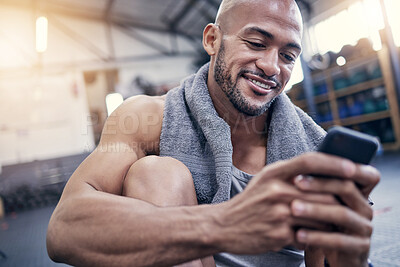 Buy stock photo Shot of a muscular young man using a cellphone while taking a break from exercising in a gym