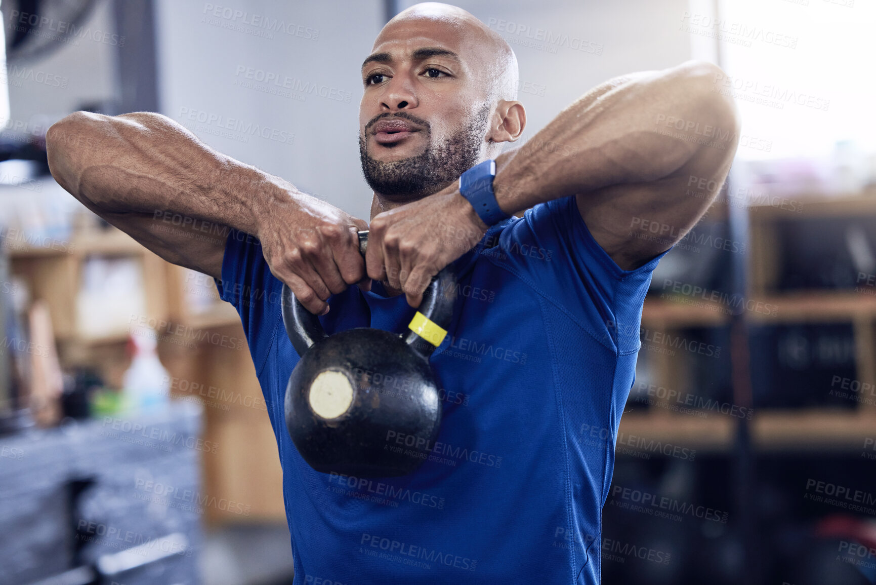 Buy stock photo Shot of a young man working out with a kettle bell at the gym