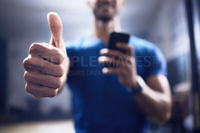 Buy stock photo Shot of an unrecognisable man showing using a smartphone and showing thumbs up in a gym