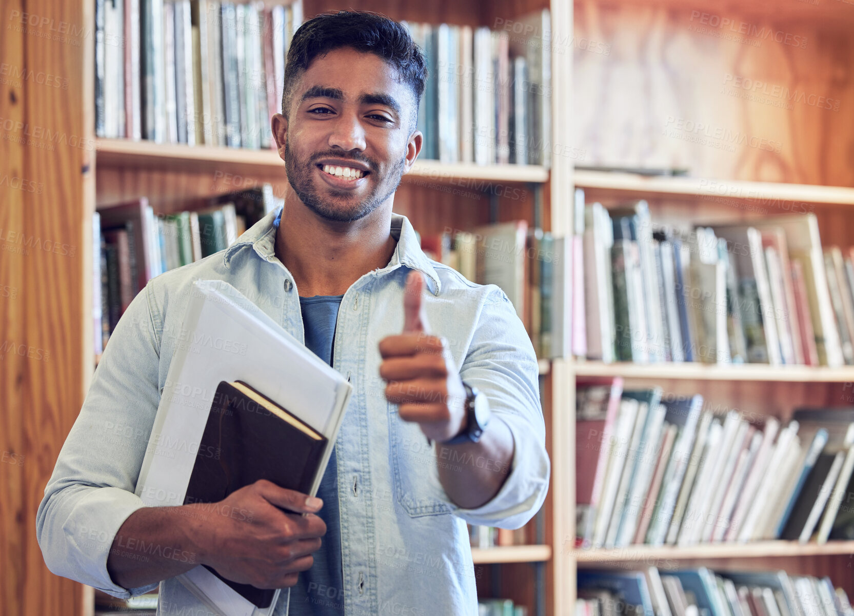 Buy stock photo Shot of a young man showing thumbs up in a library at university