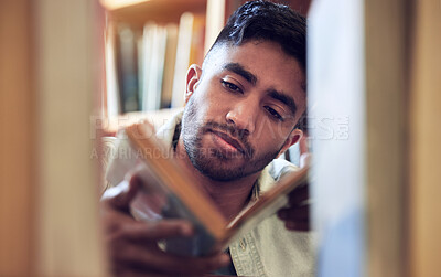 Buy stock photo Shot of a young man choosing a book to read from a library at college