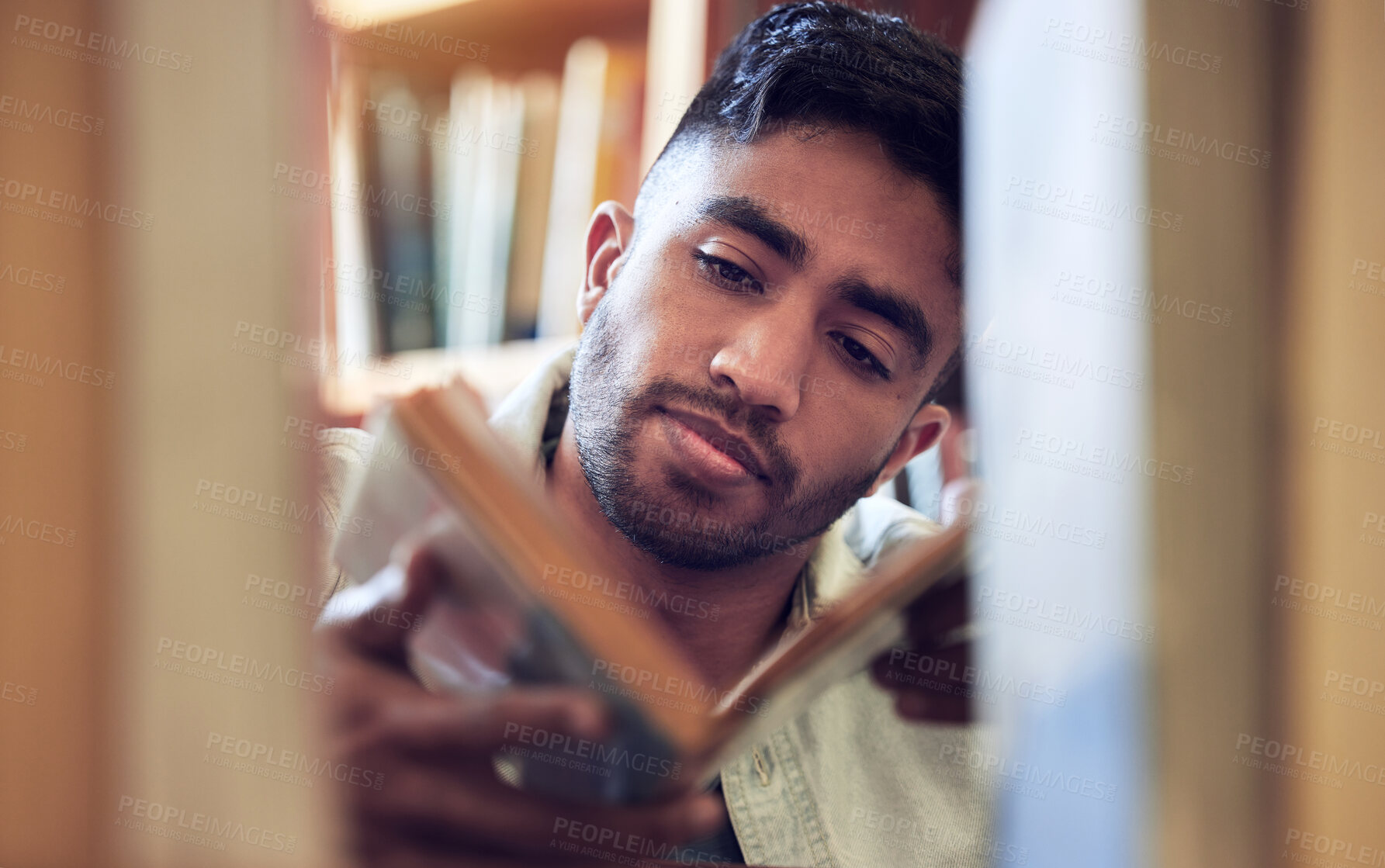 Buy stock photo Shot of a young man choosing a book to read from a library at college