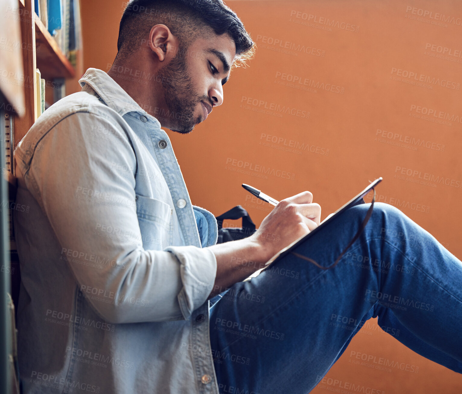 Buy stock photo Shot of a young man making notes in a library at university