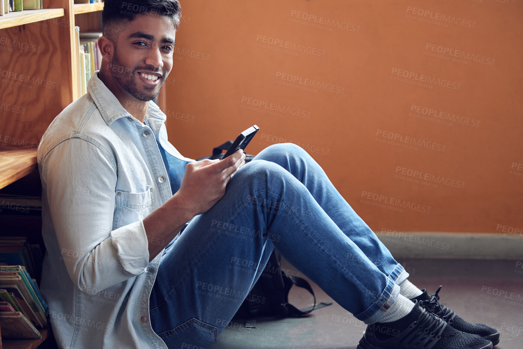 Buy stock photo Shot of a young man using a smartphone in a library at university