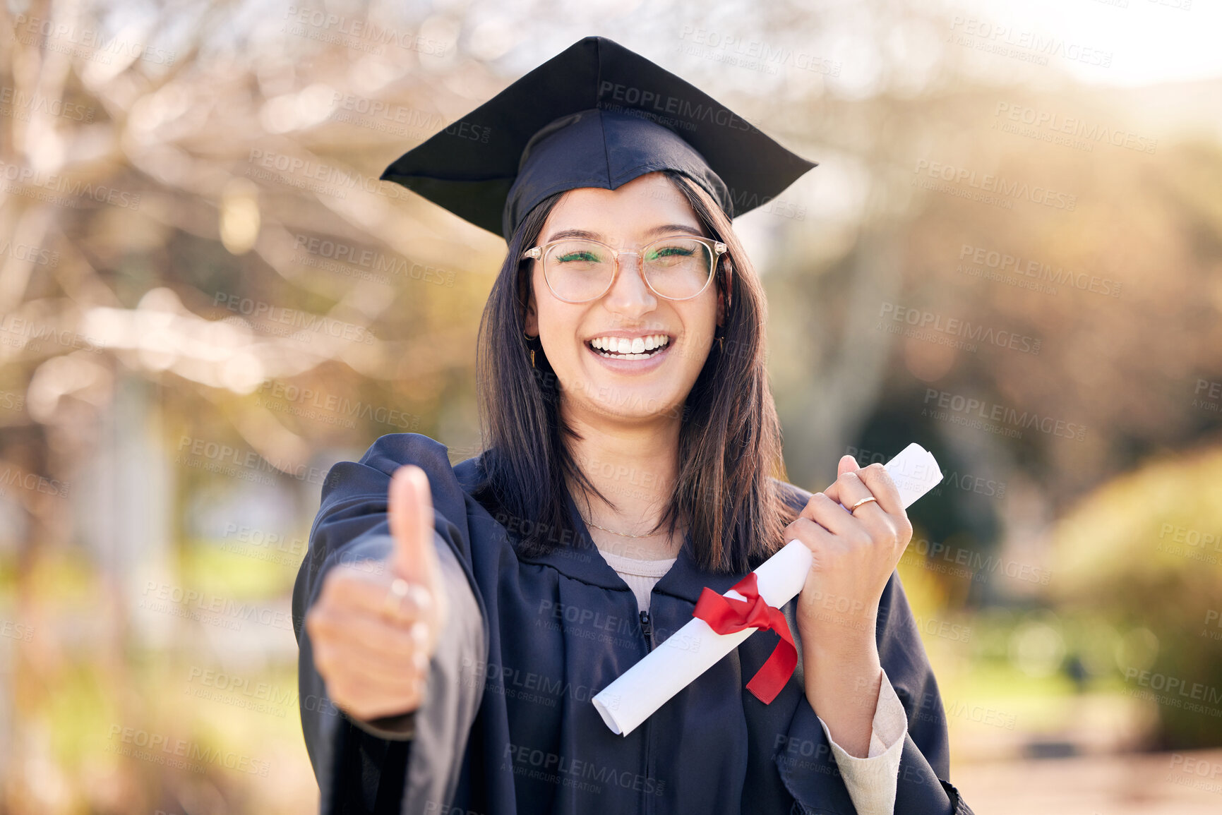 Buy stock photo Shot of a young woman showing thumbs up on graduation day