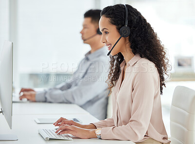 Buy stock photo Shot of a young call centre agent working on a computer in an office with her colleague in the background
