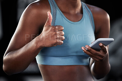 Buy stock photo Shot of a sporty young woman showing thumbs up while using her cellphone