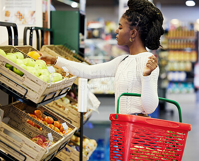 Buy stock photo Black woman, supermarket and shopping for fruit, choice or discount for health, diet or nutrition in customer experience. Plastic basket, grocery store or mall for retail, sales or girl with decision