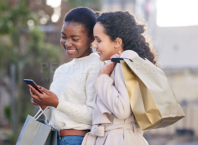Buy stock photo Shot of two friends using a smartphone during a day of shopping