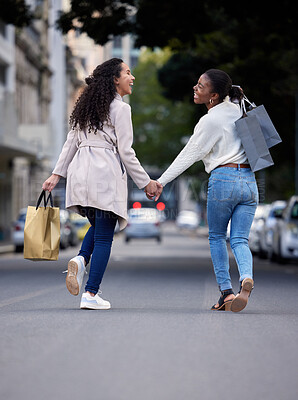 Buy stock photo Shot of two friends cheerfully walking down the street after spending the day shopping