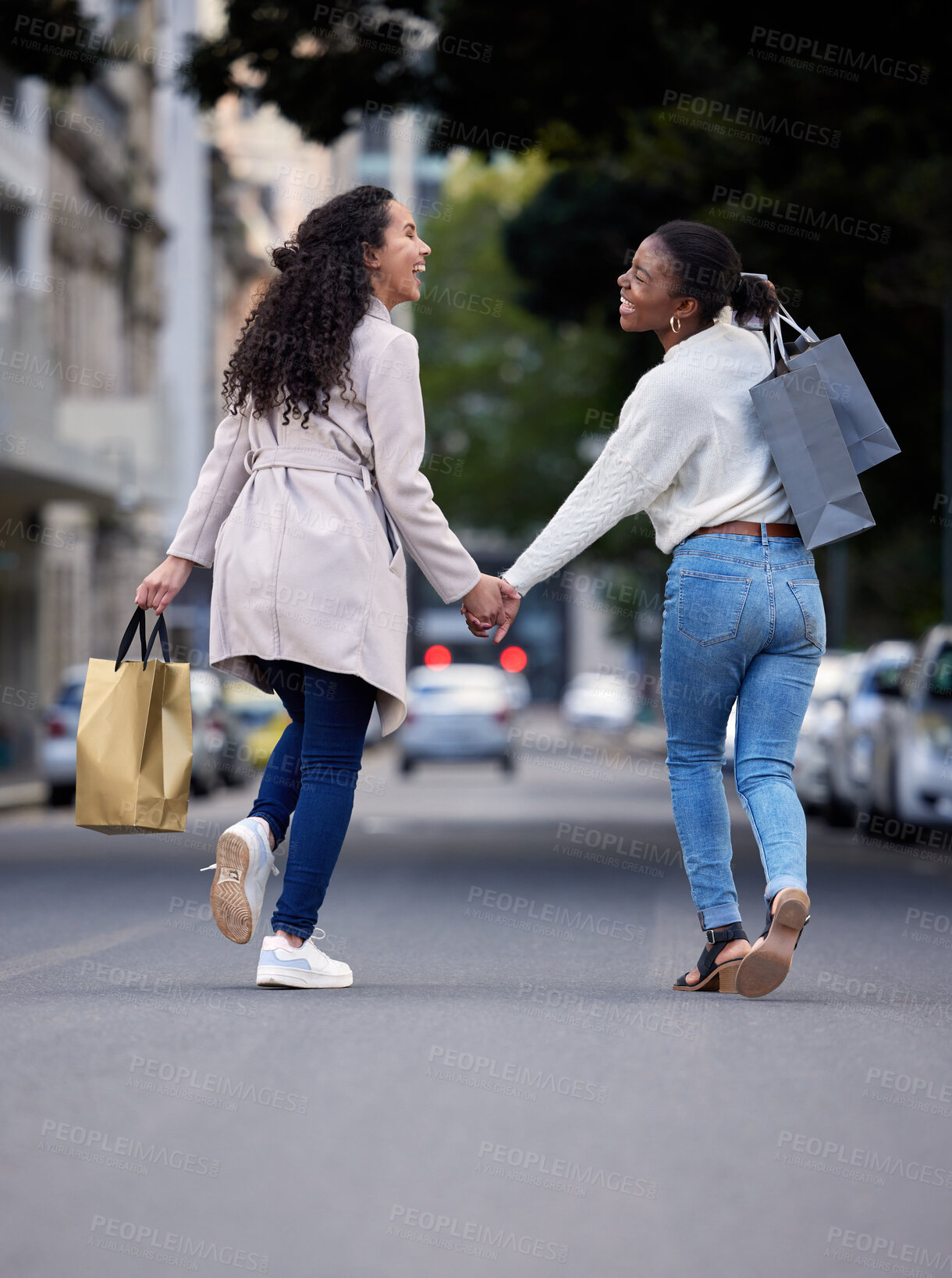 Buy stock photo Shot of two friends cheerfully walking down the street after spending the day shopping