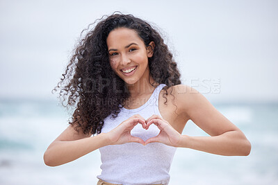 Buy stock photo Shot of a young woman making a heart gesture with her hands at the beach