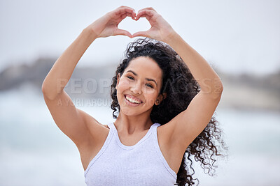 Buy stock photo Shot of a young woman making a heart gesture with her hands at the beach