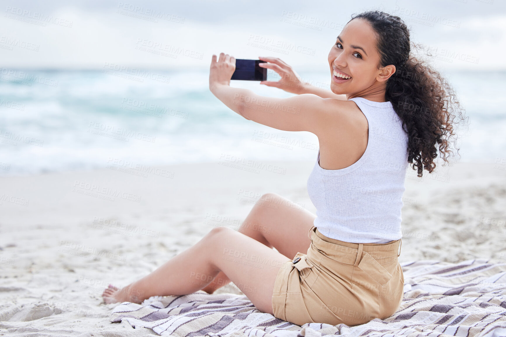 Buy stock photo Shot of a young woman taking a picture at the beach