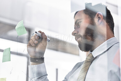 Buy stock photo Low angle shot of a young businessman writing notes on a glass wall in an office