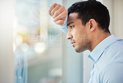 Buy stock photo Shot of a young businessman leaning against a window looking depressed