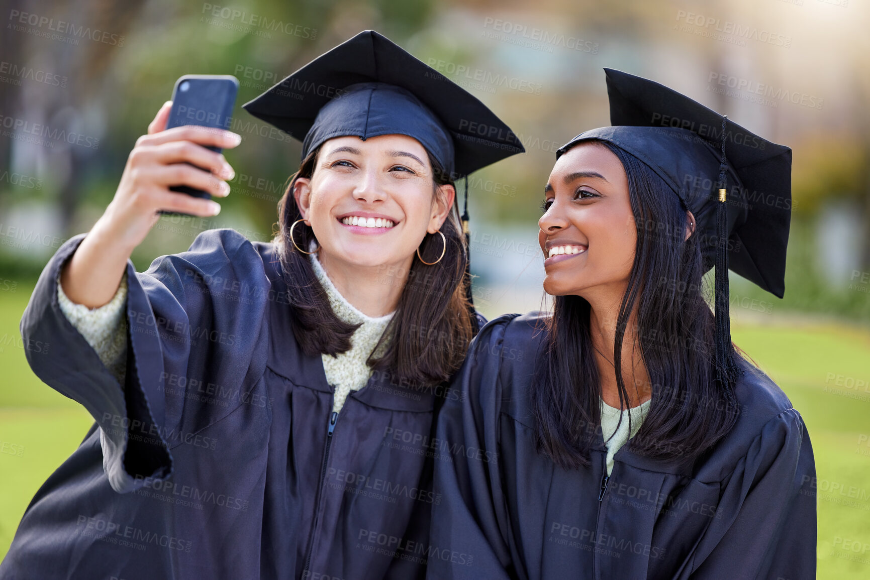 Buy stock photo Cropped shot of two attractive young female students taking selfies while celebrating on graduation day