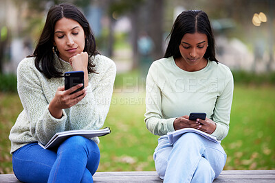 Buy stock photo Shot of two young women using their smartphones while studying at college
