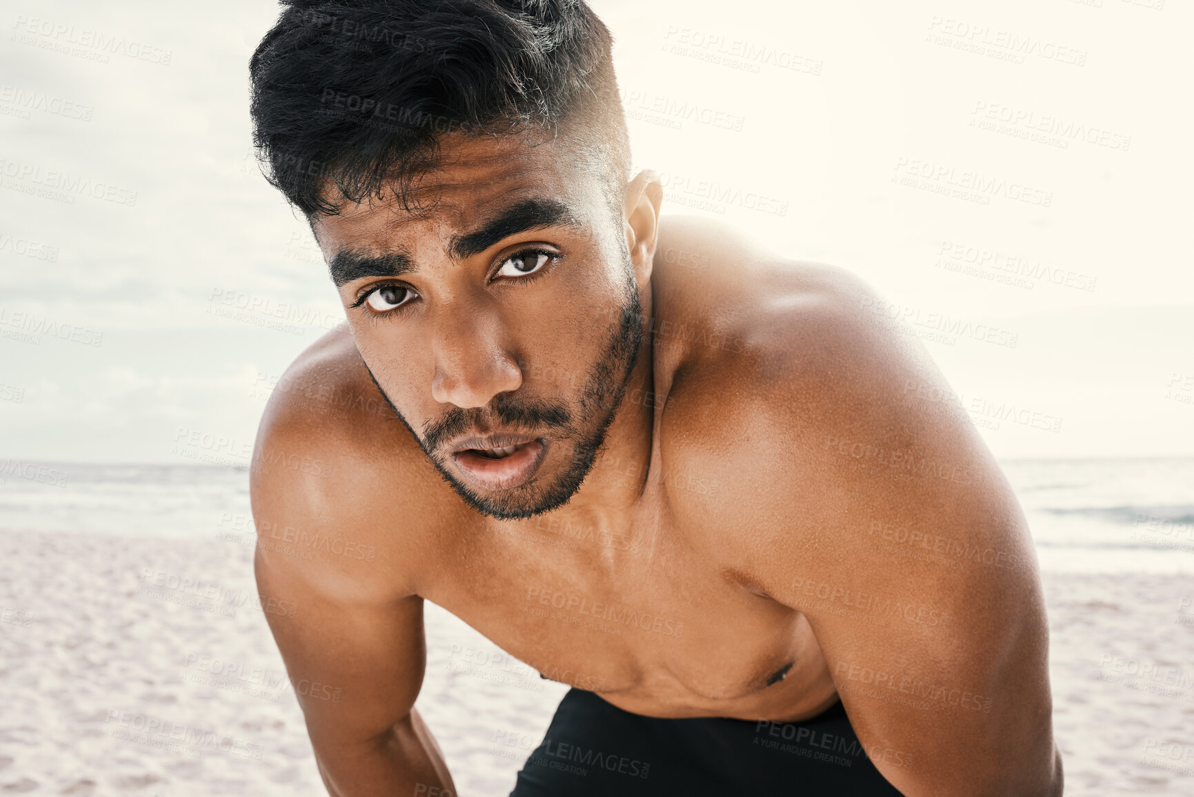 Buy stock photo Shot of an sporty young man resting with his hands on his knees while out for a run