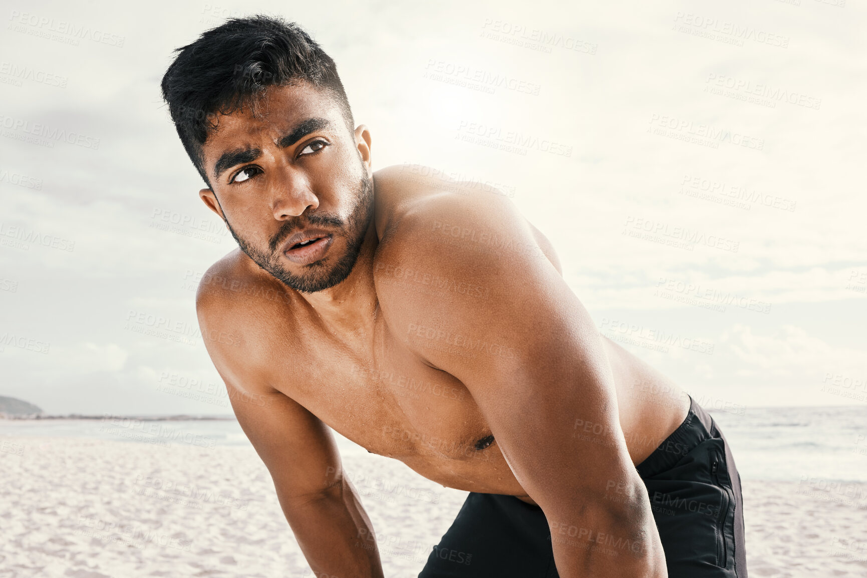 Buy stock photo Shot of an sporty young man resting with his hands on his knees while out for a run